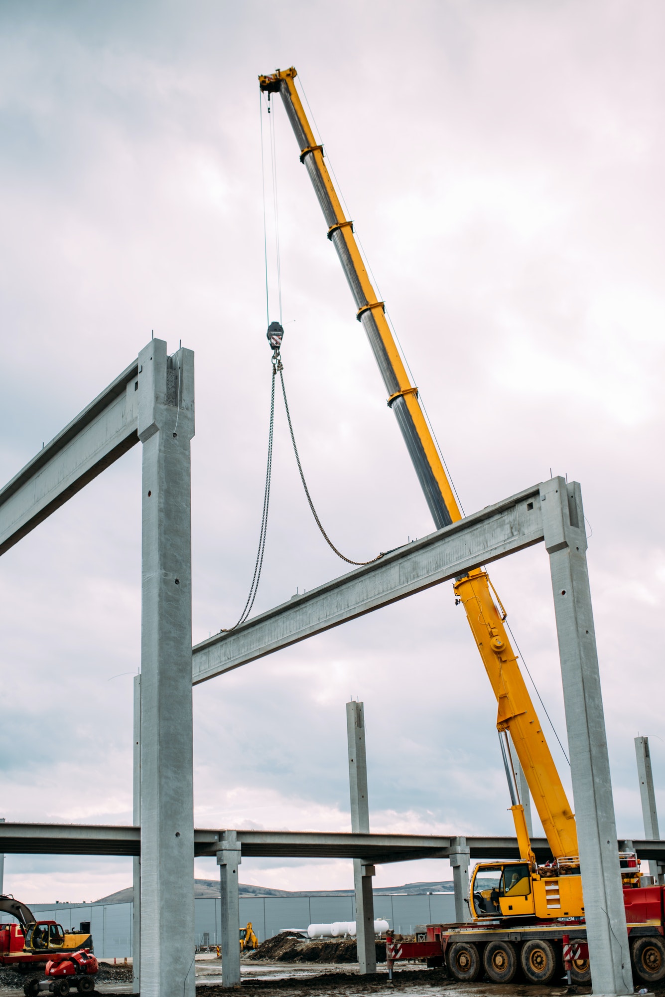 Construction site details - crane lifting a precast concrete cement beam to building assembly